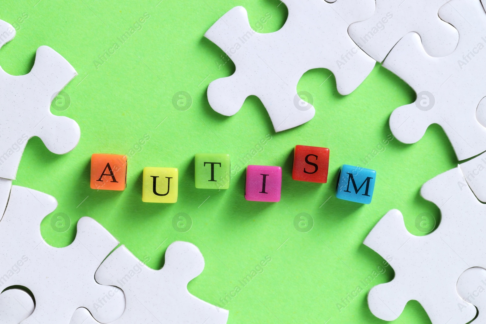 Photo of Word Autism made with colorful cubes and puzzle pieces on green background, flat lay