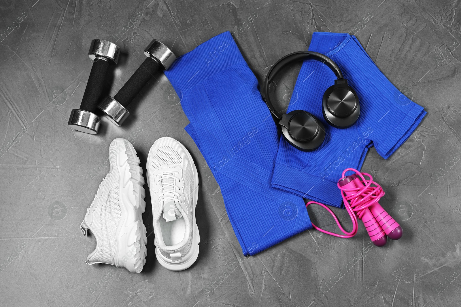 Photo of Stylish sportswear, white sneakers, dumbbells, skipping rope and headphones on grey background, flat lay