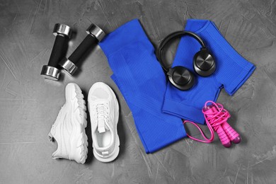 Photo of Stylish sportswear, white sneakers, dumbbells, skipping rope and headphones on grey background, flat lay