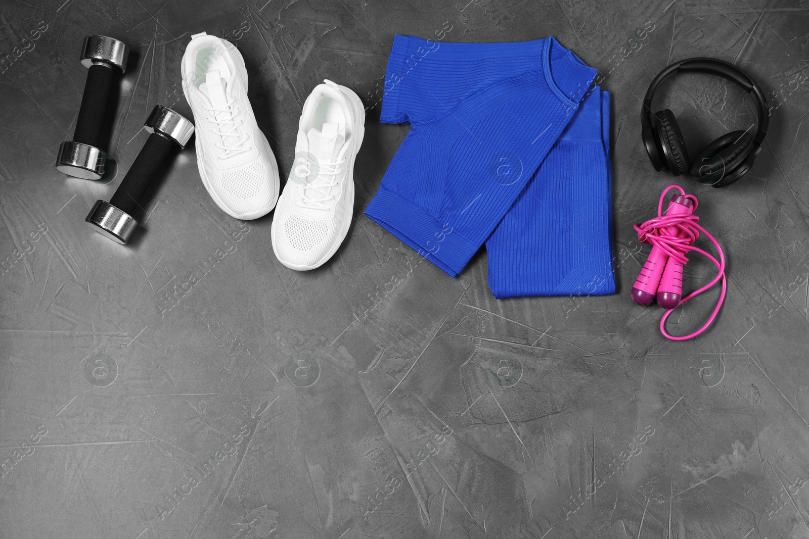 Photo of Stylish sportswear, white sneakers, dumbbells, skipping rope and headphones on grey background, flat lay. Space for text