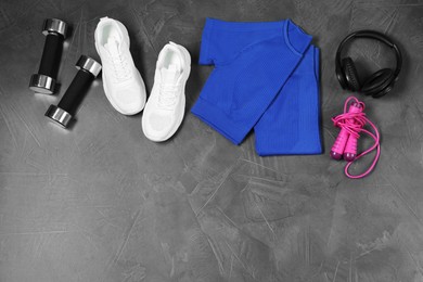 Photo of Stylish sportswear, white sneakers, dumbbells, skipping rope and headphones on grey background, flat lay. Space for text