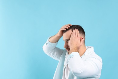 Baldness problem. Man with receding hairline on light blue background, space for text