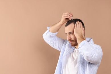 Baldness treatment. Man applying serum onto hair on beige background, space for text