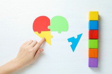 Photo of Woman playing with colorful puzzle pieces and cubes on white wooden background, top view