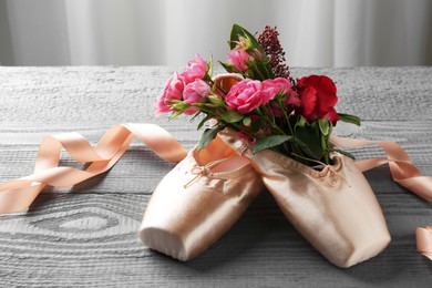 Photo of Pair of beautiful pointe shoes and flowers on grey wooden table