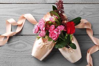 Photo of Pair of beautiful pointe shoes and flowers on grey wooden table, top view