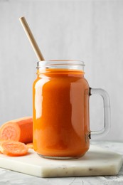 Photo of Fresh carrot juice in mason jar and vegetable on gray textured table