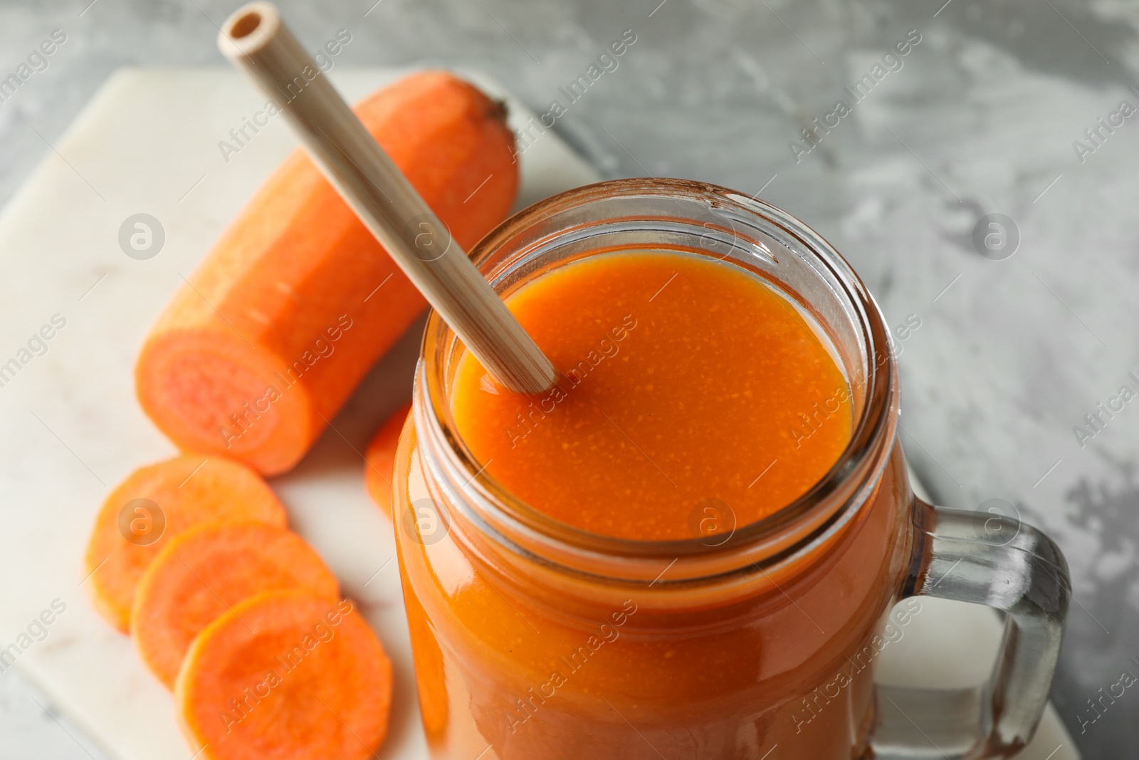 Photo of Fresh carrot juice in mason jar and vegetable on gray table, closeup