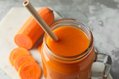 Photo of Fresh carrot juice in mason jar and vegetable on gray table, closeup