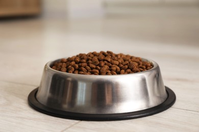 Photo of Dry pet food granules in feeding bowl on floor indoors, closeup