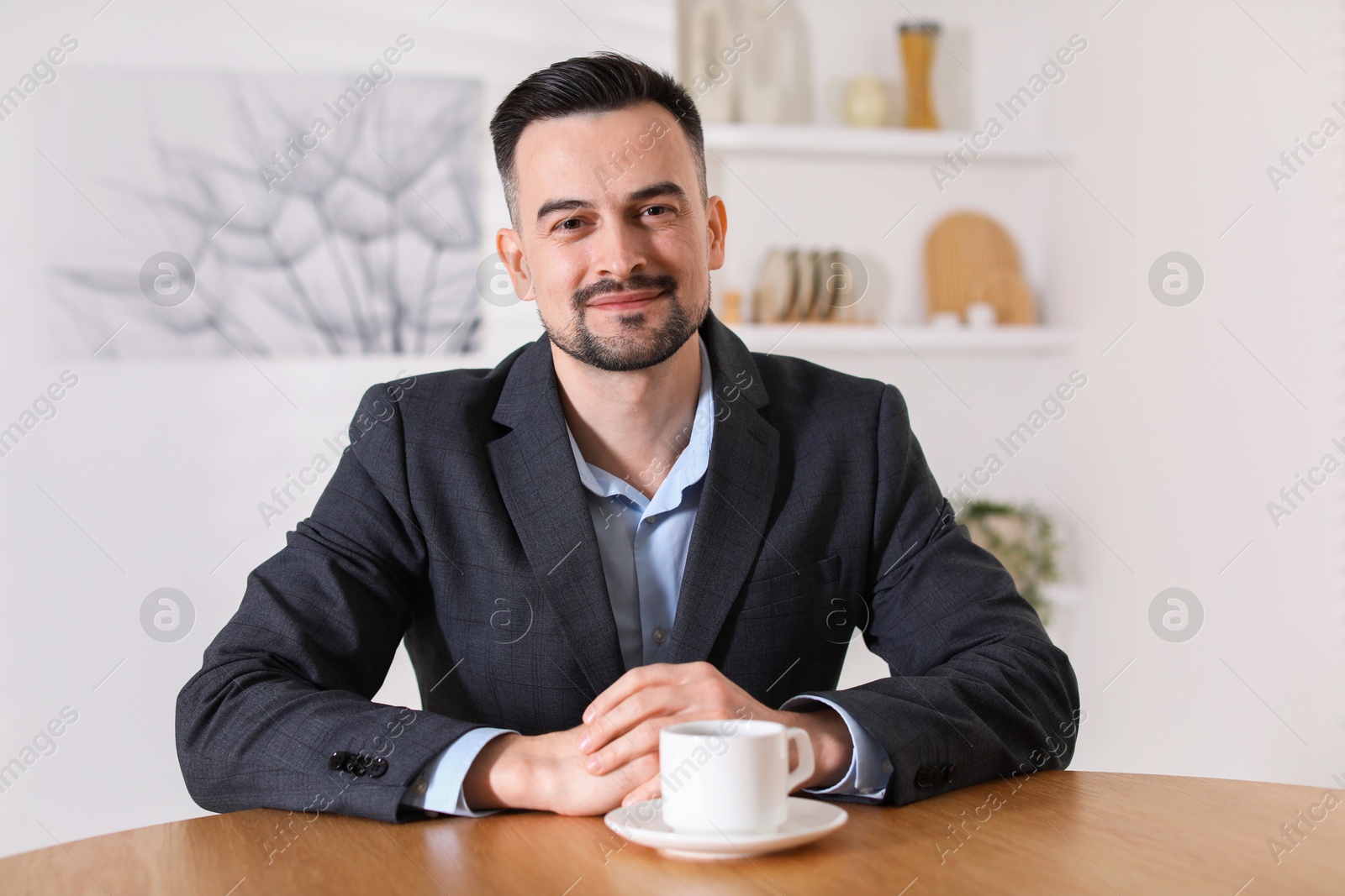 Photo of Handsome middle aged man with cup of drink at table indoors