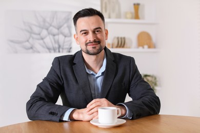 Photo of Handsome middle aged man with cup of drink at table indoors