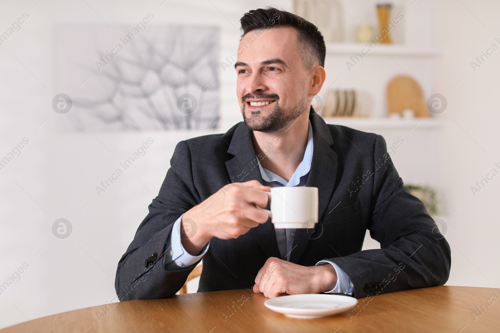 Photo of Handsome middle aged man with cup of drink at table indoors