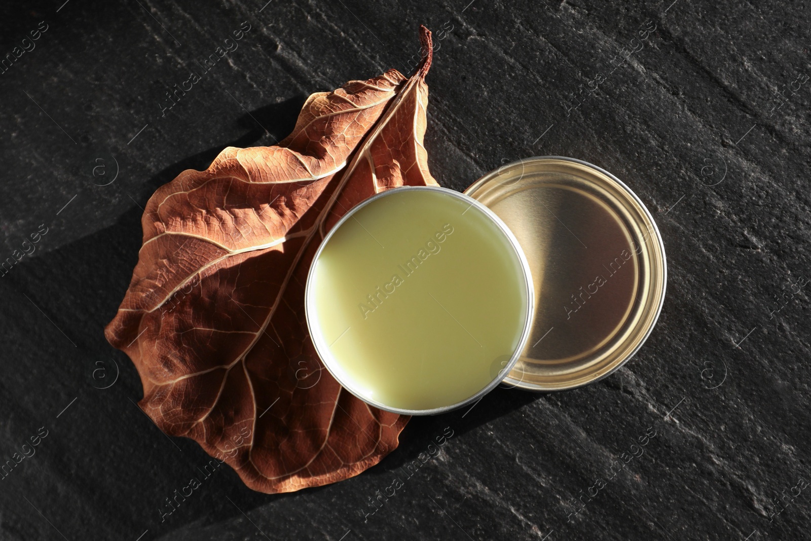 Photo of Natural solid perfume and dry leaf on black table, top view