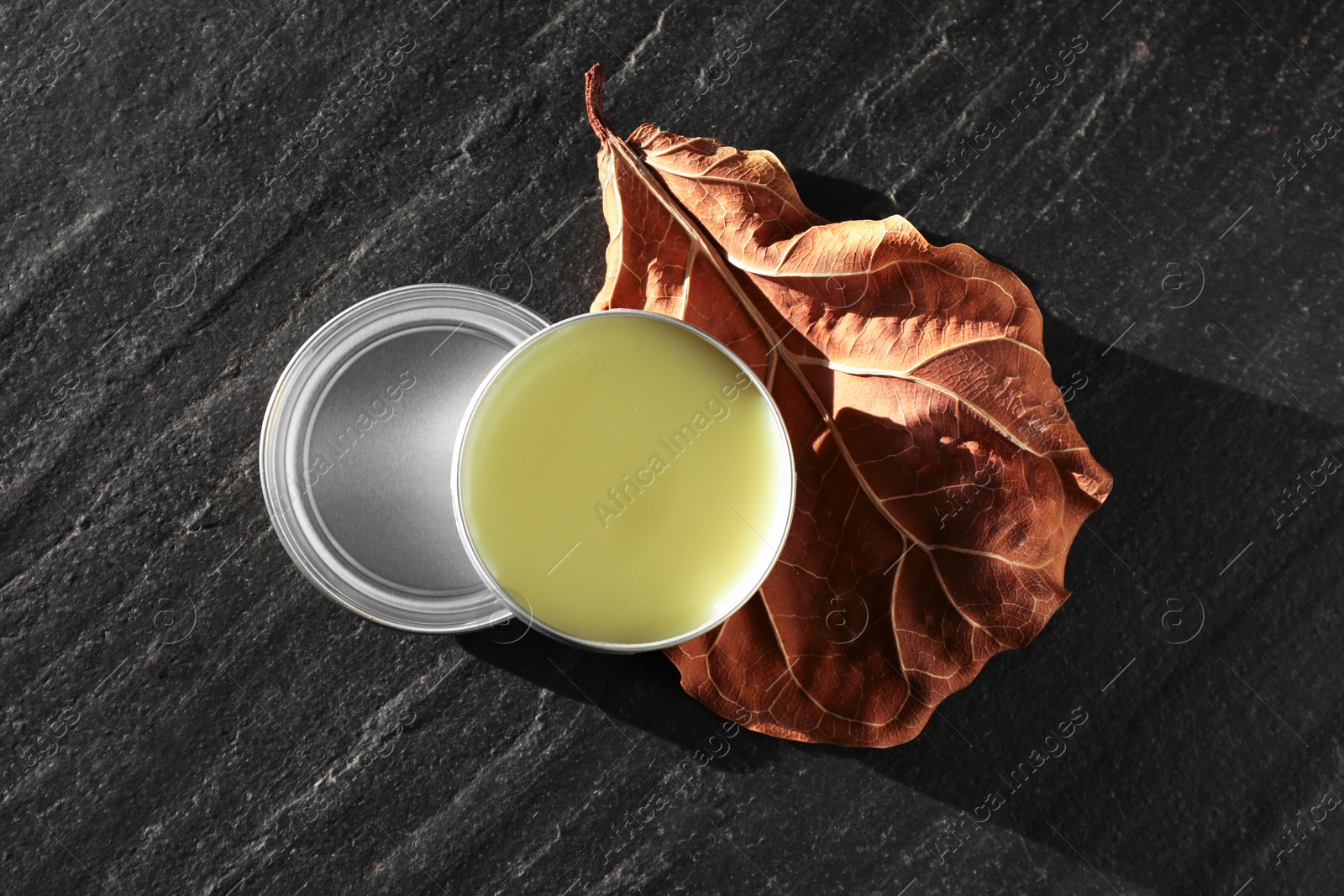 Photo of Natural solid perfume and dry leaf on black table, top view