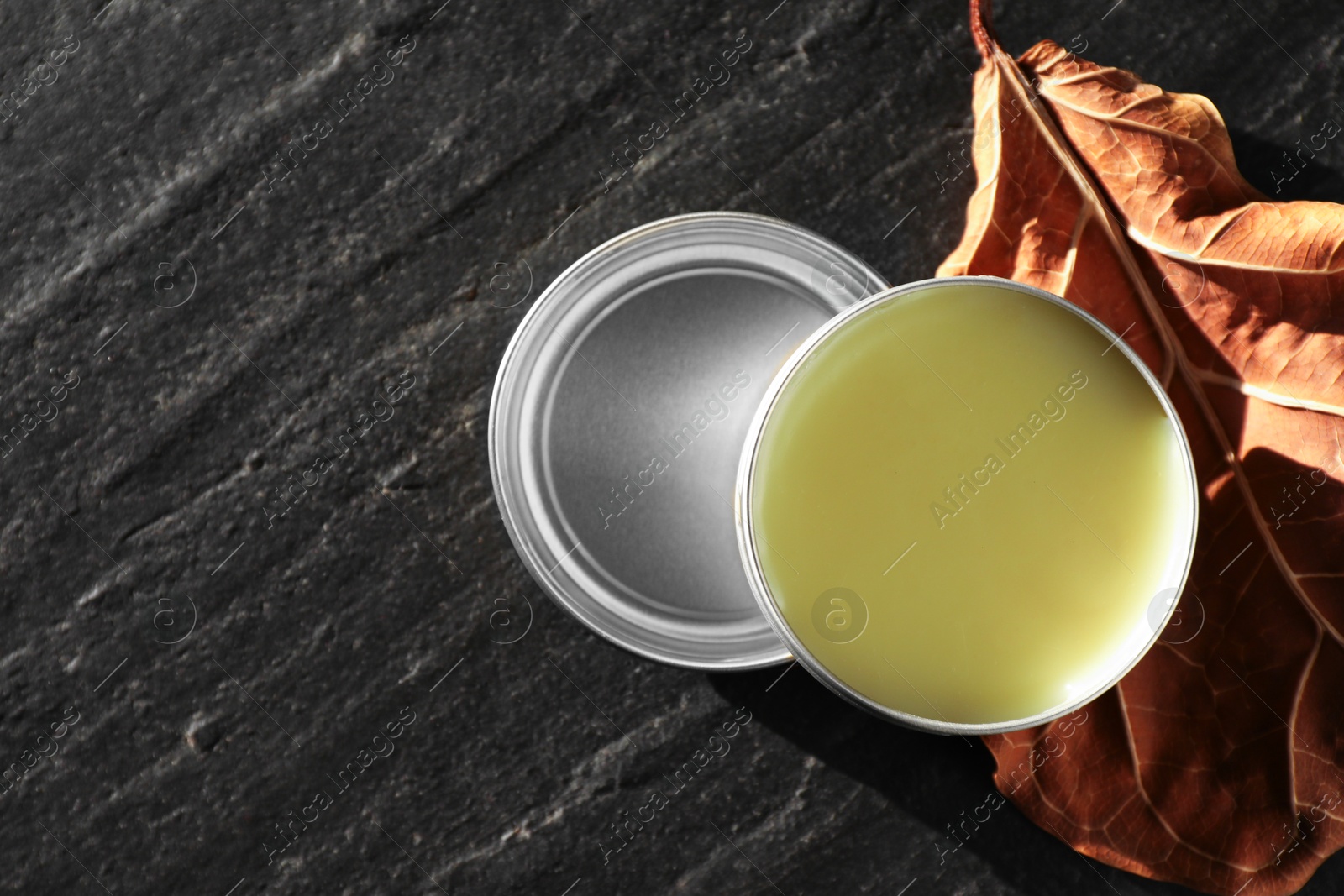 Photo of Natural solid perfume and dry leaf on black table, top view. Space for text