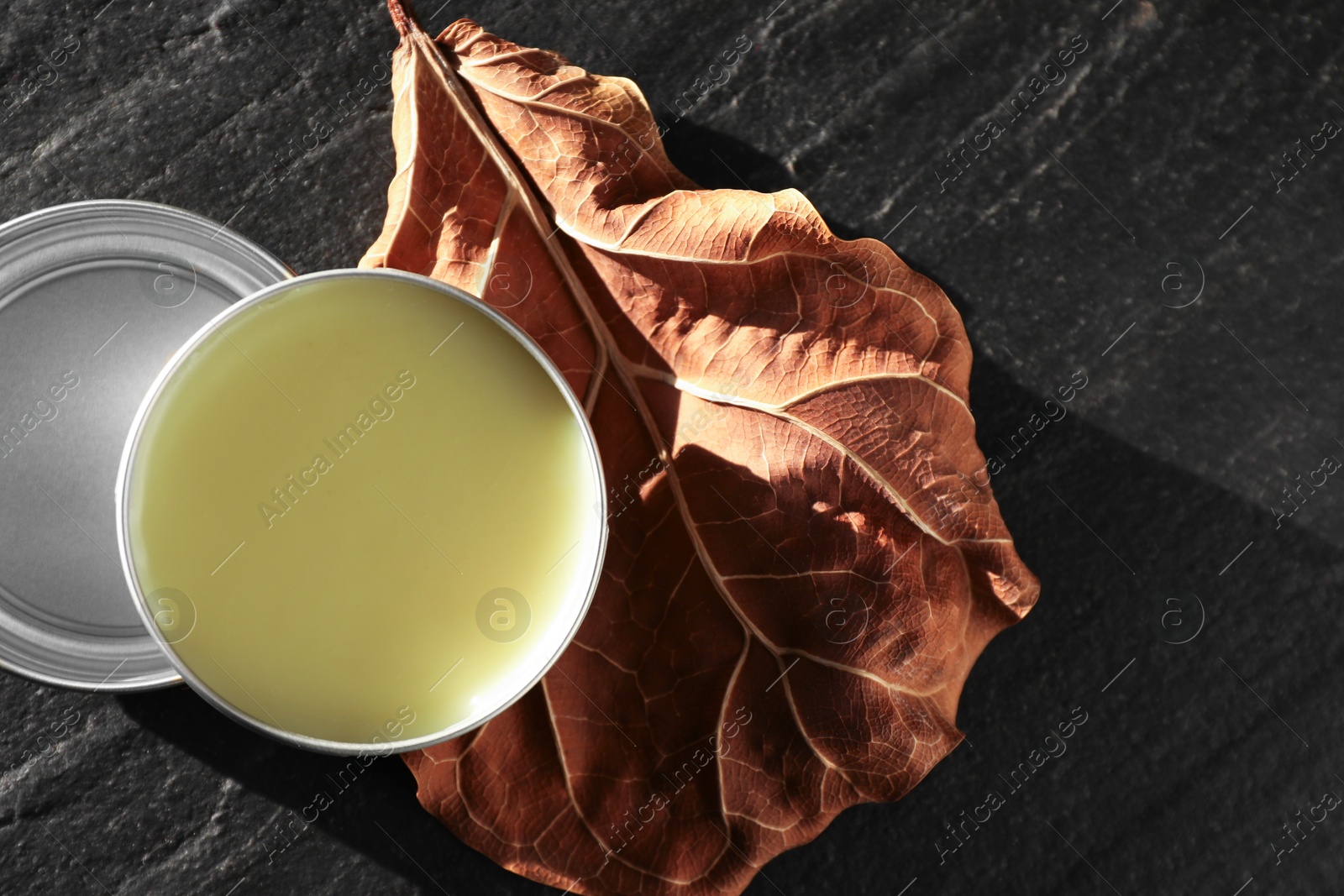 Photo of Natural solid perfume and dry leaf on black table, top view