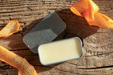 Photo of Natural solid perfume in container and orange peels on wooden table, flat lay