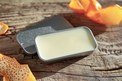 Photo of Natural solid perfume in container and orange peels on wooden table, closeup