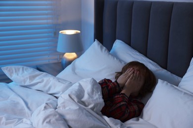 Photo of Scared boy covering face with hands in bed at night