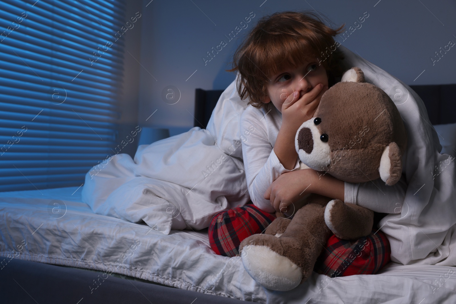 Photo of Scared boy with teddy bear in bed at night. Space for text