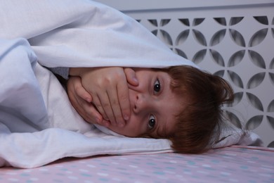 Photo of Afraid boy under blanket on bed at night