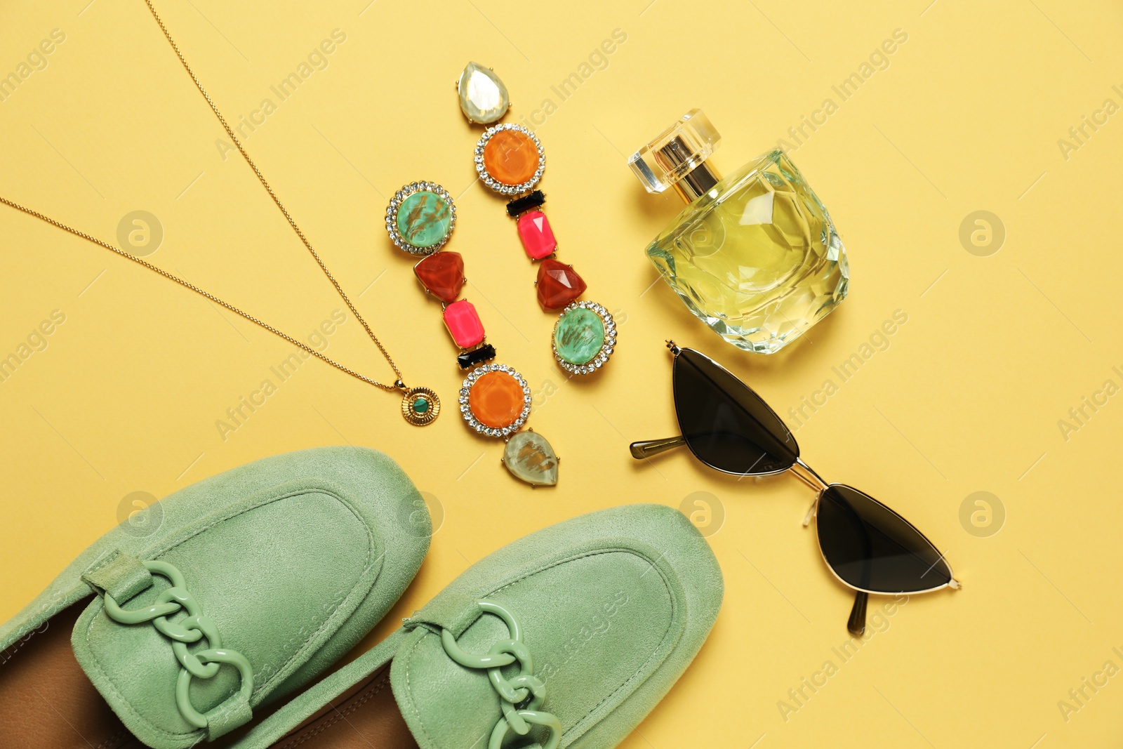 Photo of Stylish jewelry, accessories, perfume and shoes on pale yellow background, flat lay