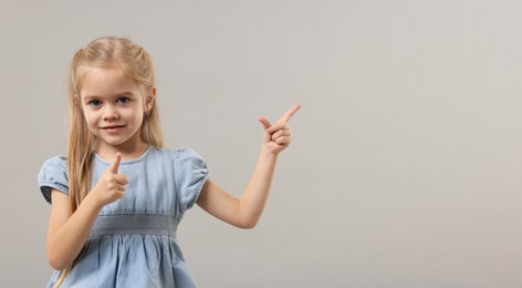 Photo of Cute little girl pointing at something on gray background. Space for text