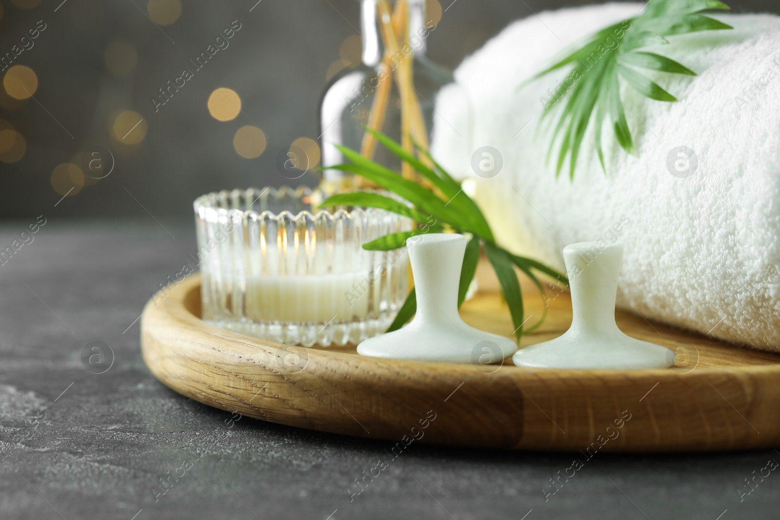 Photo of Spa stones, burning candle, towel and green leaves on grey table, closeup