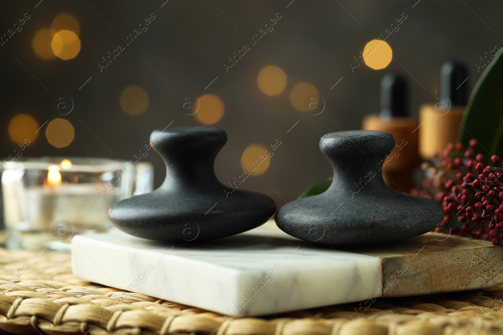 Photo of Spa stones, floral decor and candle on wicker mat, closeup