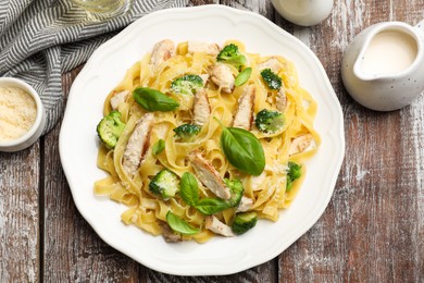 Photo of Delicious pasta Alfredo with chicken served on wooden table, flat lay