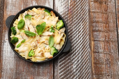 Photo of Delicious pasta Alfredo with chicken, cheese, creamy sauce, broccoli and basil on wooden table, top view. Space for text