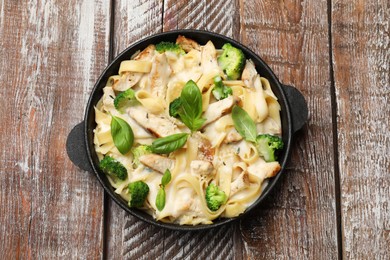 Photo of Delicious pasta Alfredo with chicken, cheese, creamy sauce, broccoli and basil on wooden table, top view