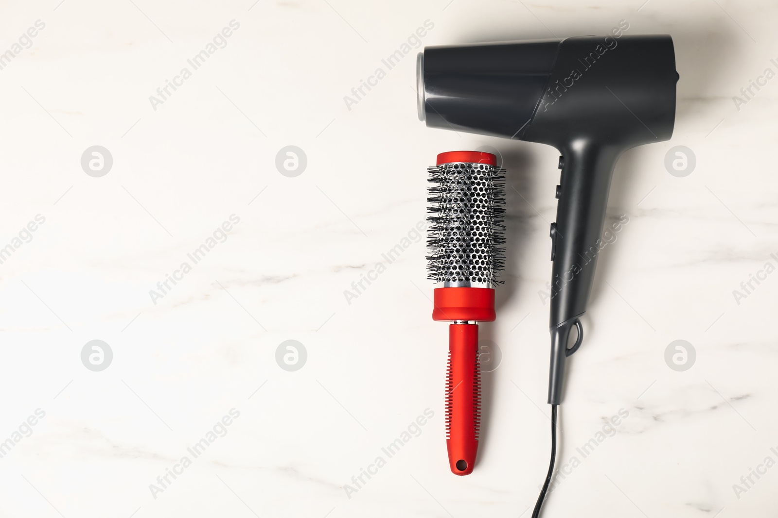 Photo of Stylish round hair brush and hairdryer on white marble table, top view. Space for text