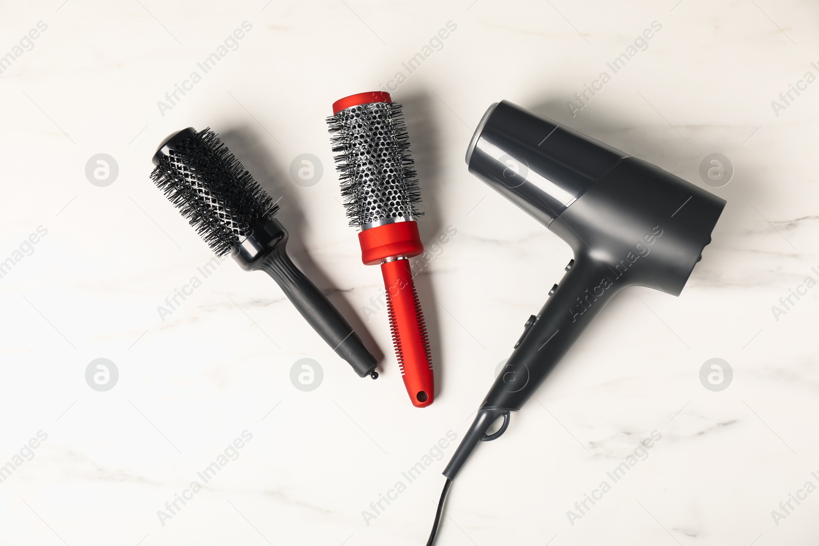 Photo of Stylish round hair brushes and hairdryer on white marble table, flat lay