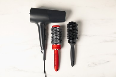 Photo of Stylish round hair brushes and hairdryer on white marble table, flat lay