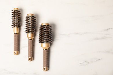 Photo of Stylish round hair brushes on white marble table, flat lay. Space for text