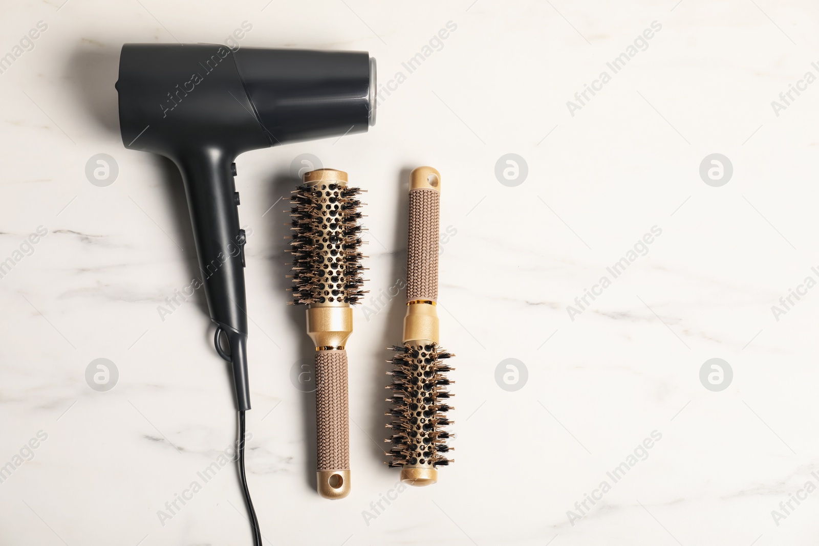 Photo of Stylish round hair brushes and hairdryer on white marble table, flat lay. Space for text