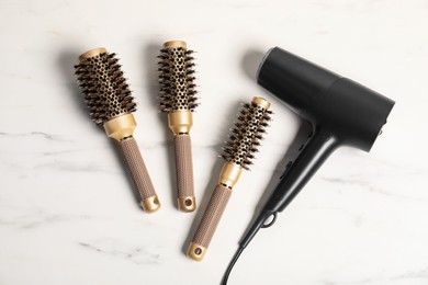 Photo of Stylish round hair brushes and hairdryer on white marble table, flat lay