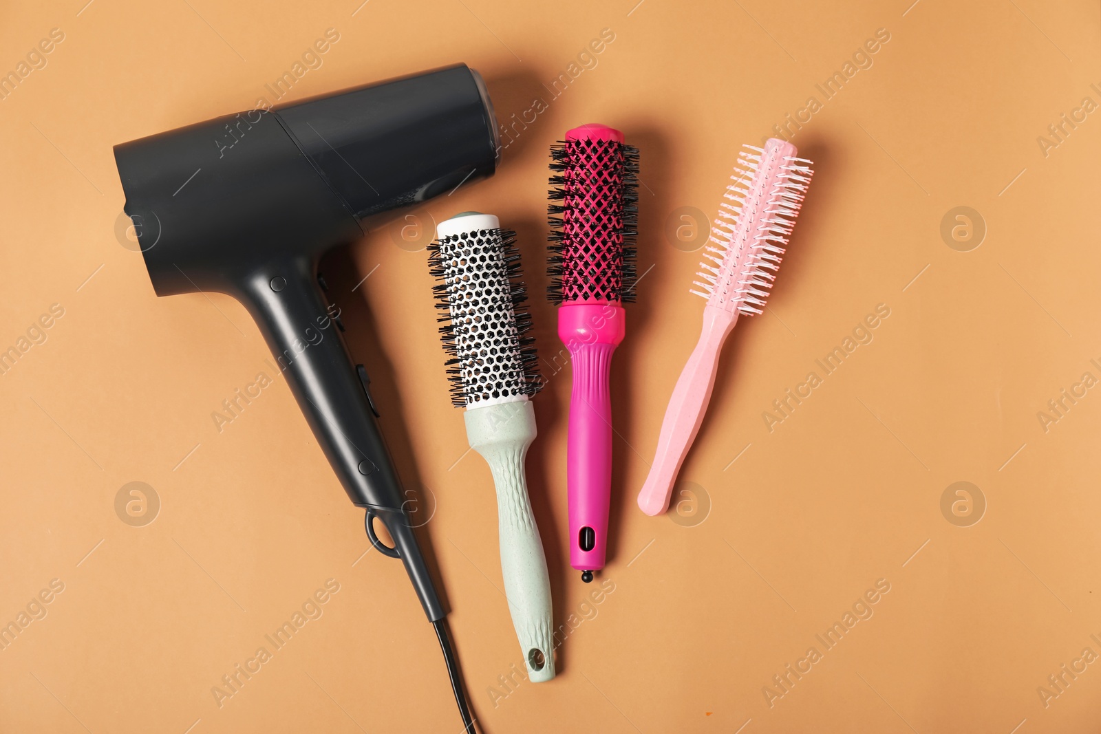 Photo of Stylish round hair brushes and hairdryer on light brown background, flat lay