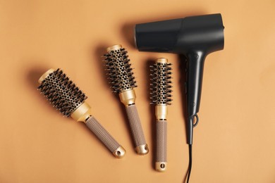 Photo of Stylish round hair brushes and hairdryer on light brown background, flat lay