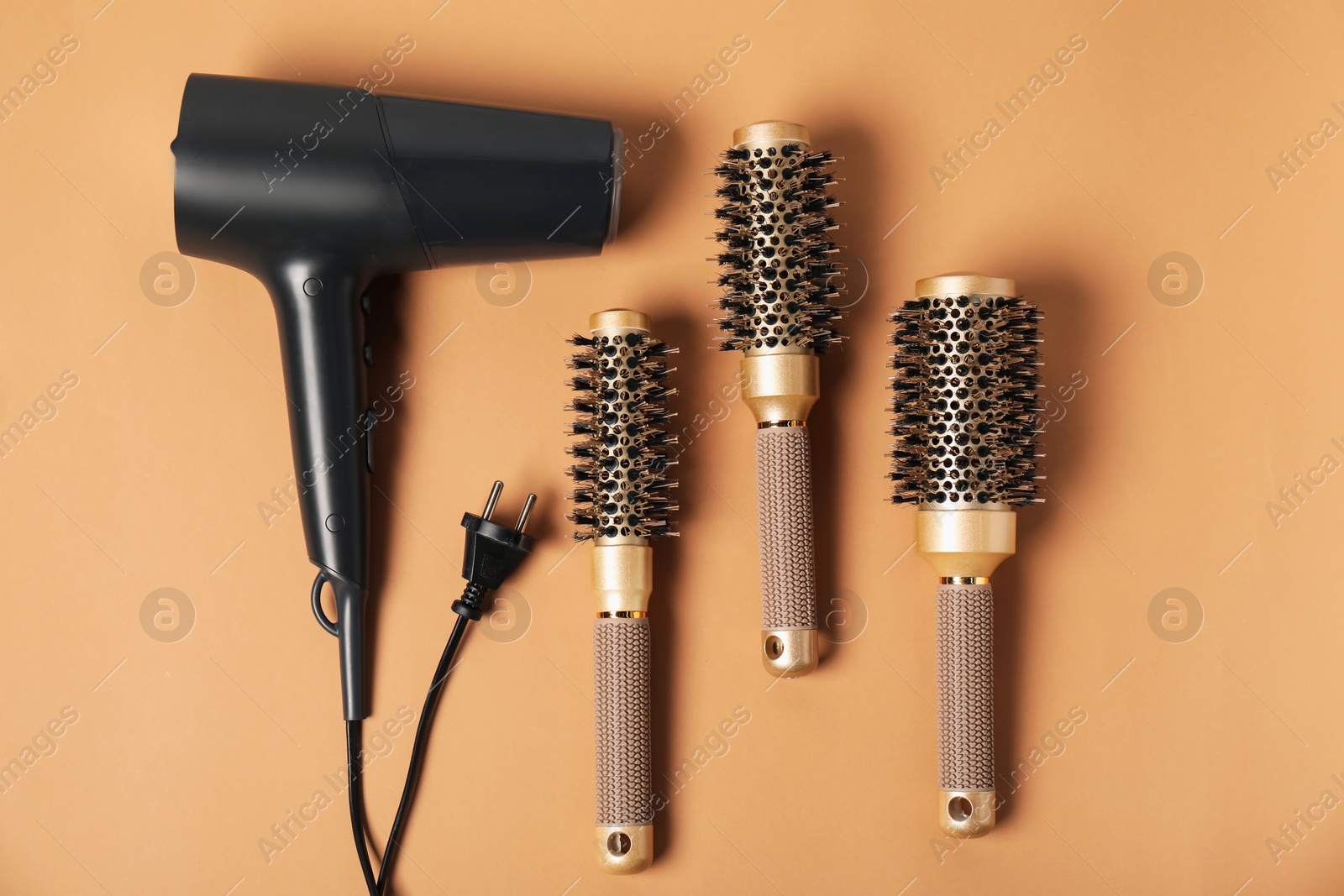 Photo of Stylish round hair brushes and hairdryer on light brown background, flat lay