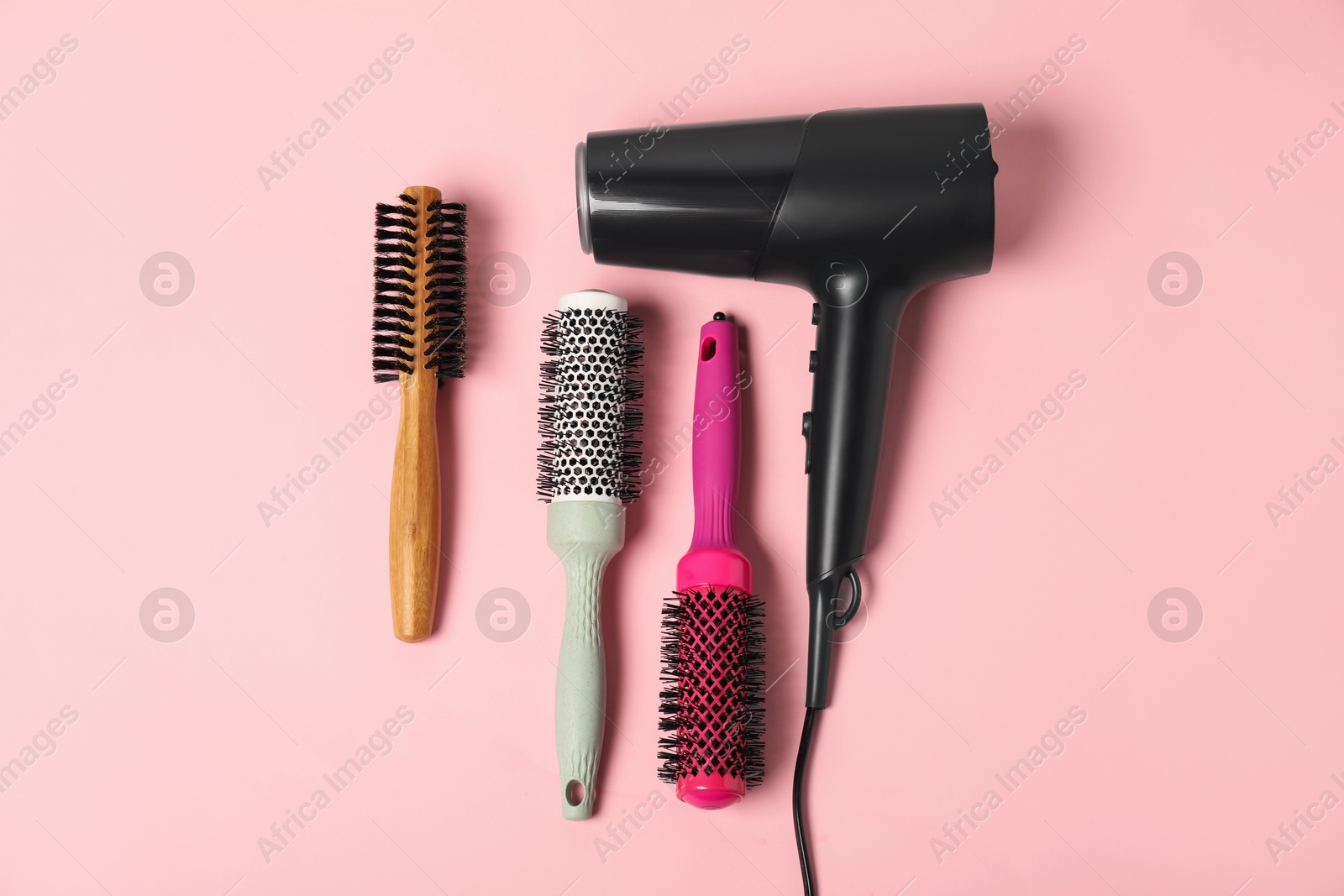 Photo of Stylish round hair brushes and hairdryer on pink background, flat lay