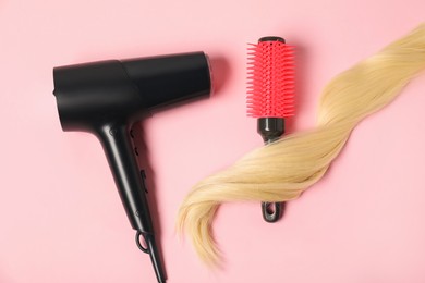 Photo of Stylish round brush, lock of blonde hair and hairdryer on pink background, flat lay