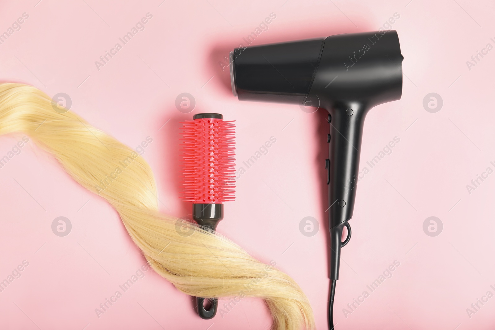 Photo of Stylish round brush, lock of blonde hair and hairdryer on pink background, flat lay