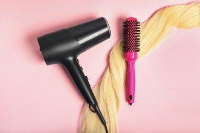 Photo of Stylish round brush, lock of blonde hair and hairdryer on pink background, flat lay