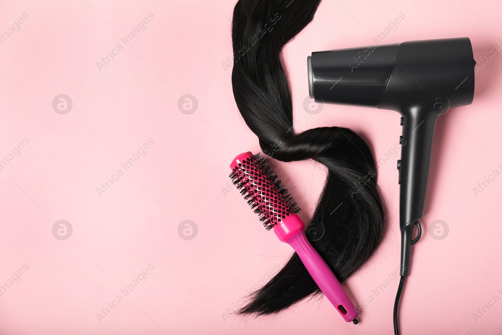 Photo of Stylish round brush, lock of black hair and hairdryer on pink background, flat lay. Space for text