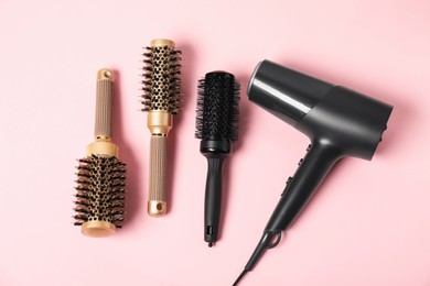 Photo of Stylish round hair brushes and hairdryer on pink background, flat lay