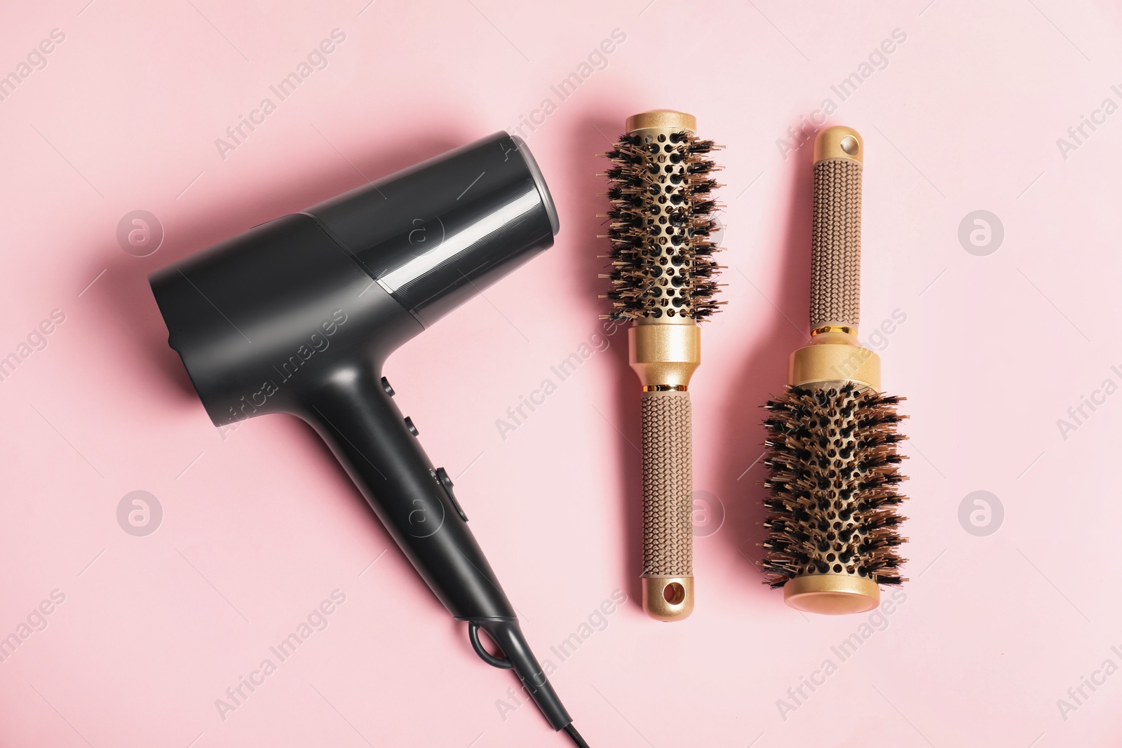 Photo of Stylish round hair brushes and hairdryer on pink background, flat lay