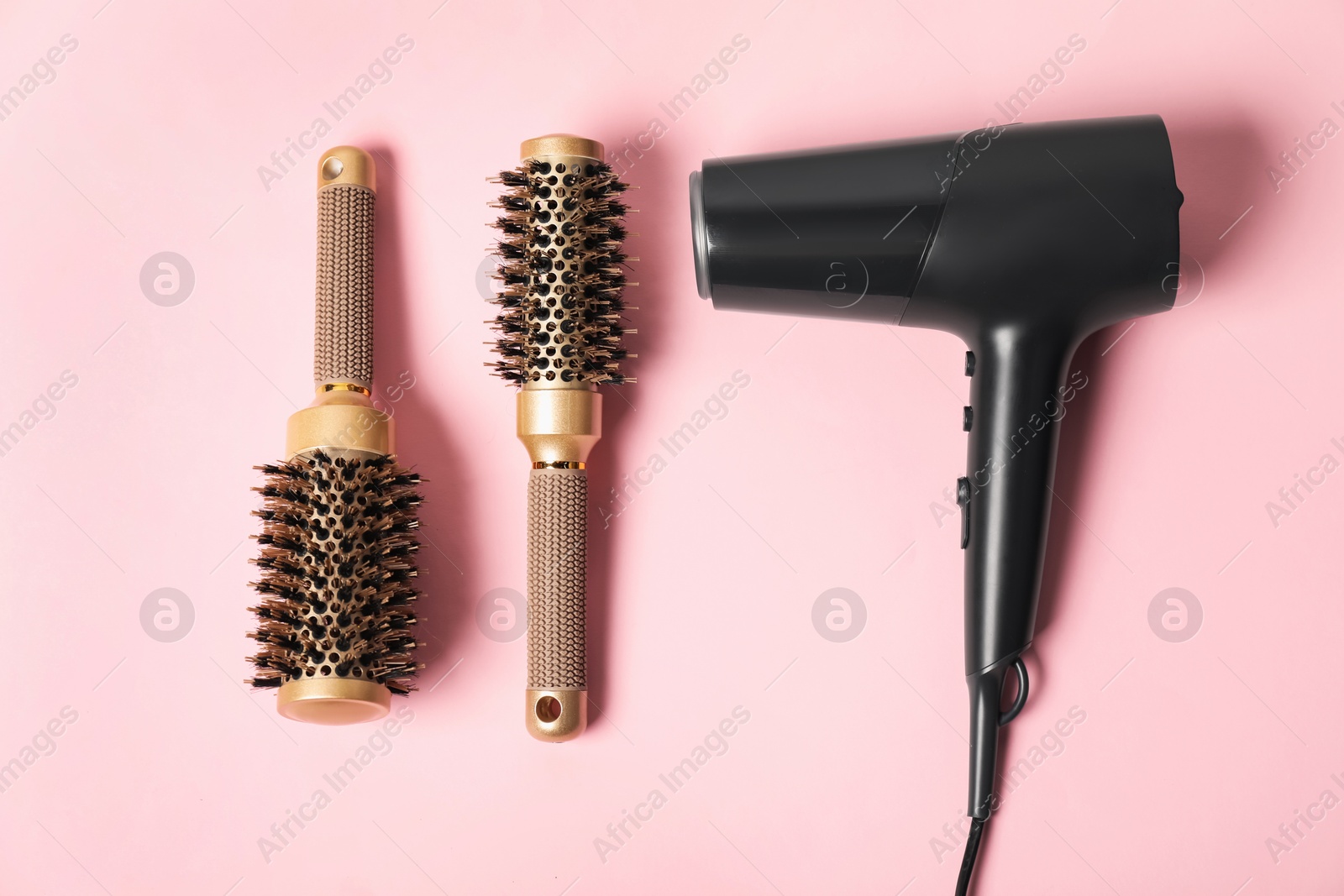 Photo of Stylish round hair brushes and hairdryer on pink background, flat lay